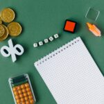 Flat lay of tax-related items on green background including coins, notebook, and calc.
